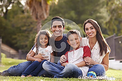 Happy young Hispanic family sitting the on grass in the park smiling to camera, close up Stock Photo