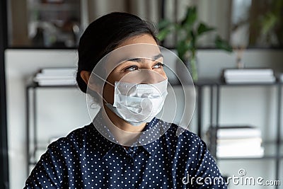 Happy young indian female manager in protective mask looking away. Stock Photo