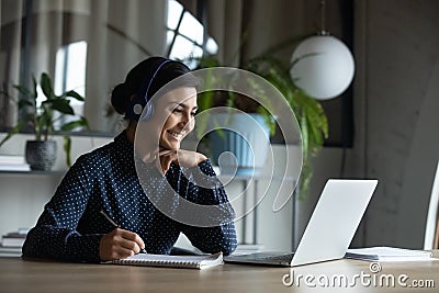 Happy young indian girl with headphones looking at laptop screen. Stock Photo