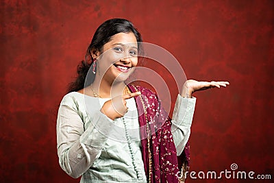 Happy young indian Girl looking camera by showing empty hand and pointing finger - concept of product sales, promotions, offers Stock Photo