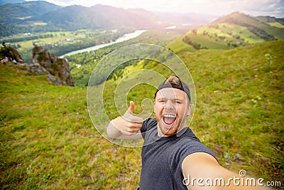 Happy young man blogger on background of mountains in summer sunset. Lifestyle Russia Altay traveler makes selfie photo Stock Photo