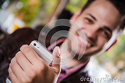 Happy young man browsing internet on smartphone sitting at outdoor cafe. Selective focus. Stock Photo