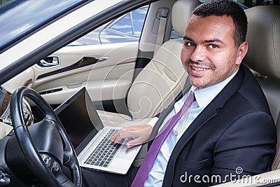 Happy young man in business suit sits in driver`s seat in car with laptop. Working with a laptop in the car Stock Photo