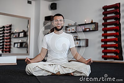 Happy young man with positive smile with a beard practicing yoga in the fitnes studio. Healthy lifestyle Stock Photo