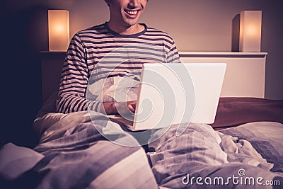 Happy young man is sitting in bed and chatting on webcam Stock Photo
