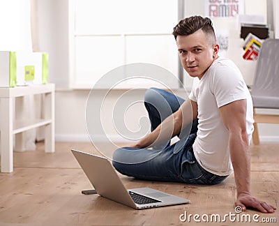 Happy young man sitting on living room floor, using laptop, smiling Stock Photo