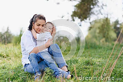 Happy young mother is playing with her baby in a park on a green lawn. Happiness and harmony of family life. Great family vacation Stock Photo