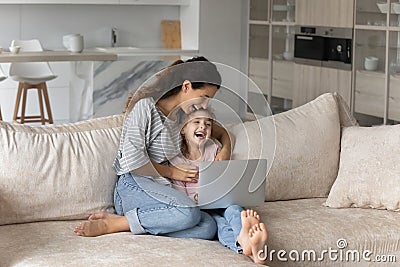 Happy young mother and small daughter watching funny cartoons. Stock Photo