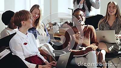 Happy young multiethnic business women sit together listening to corporate seminar laughing at modern office conference. Stock Photo
