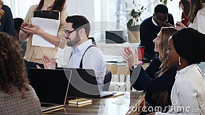 Happy young multiethnic office managers team clapping after corporate training seminar sitting at table together. Stock Photo