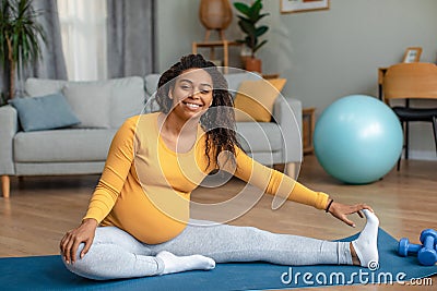 Happy young pregnant african american woman with big belly doing exercises and practicing yoga in living room Stock Photo