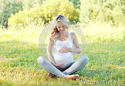 Happy young pregnant woman sitting on grass doing yoga in summer Stock Photo