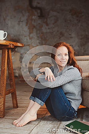 Happy young readhead woman drinking hot coffee or tea at home. Calm and cozy weekend in winter Stock Photo