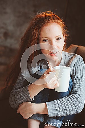 Happy young readhead woman drinking hot coffee or tea at home Stock Photo