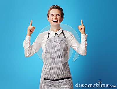 Happy young scrubwoman pointing up at copy space on blue Stock Photo