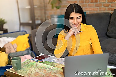 Happy young spanish lady planning summer vacation with map and laptop, choosing best travel routes for future trip Stock Photo