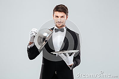 Happy young waiter lifting metal cloche from serving tray Stock Photo