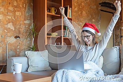 Happy young woman with arms outstretched glasses and Santa hat sitting on the sofa at home Stock Photo