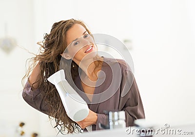 Happy young woman blow drying hair in bathroom Stock Photo