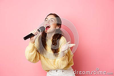 Happy young woman enjoying playing karaoke, singing in mic, looking aside at screen with lyrics, smiling cheerful Stock Photo