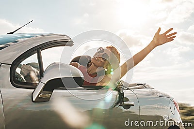 Happy young woman enjoying a ride in a convertible car. hand greeting. concept of road travel and adventure. riding with Stock Photo