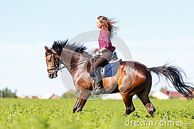 Happy young woman galloping horseback on field Stock Photo