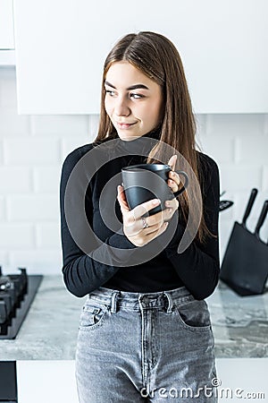 Happy young woman holding a cup of coffee in her kitchen Stock Photo