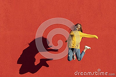 Happy young woman jumping midair in front of red wall. Stock Photo