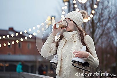 Happy young woman in knitted sweater and hat is going skating and drinks coffee Stock Photo