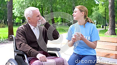 Happy young woman listening to music with old disabled man, supporting patient Stock Photo