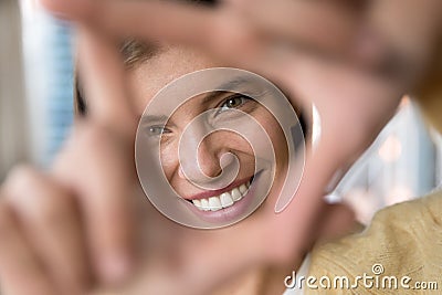 Happy young woman looking at camera through finger photo frame Stock Photo