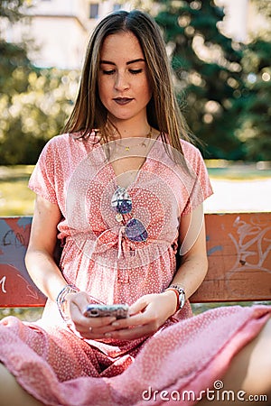 Happy young woman in a pink dress sitting on a bench watching mobile. Female having good news. Illusioned woman Stock Photo