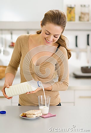 Happy young woman pouring milk into glass Stock Photo