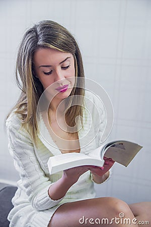 Happy young woman reading storybook on couch at home, winter, coziness, leisure and people concept - close up of young woman Stock Photo