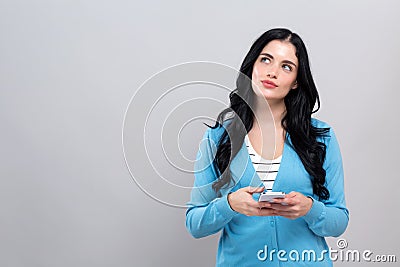Happy young woman with smart phone thinking about something Stock Photo