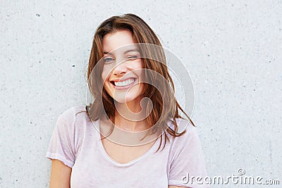 Happy young woman smiling and winking against gray wall Stock Photo