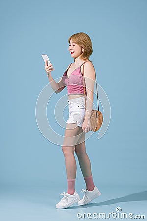 Happy young woman using mobile cell phone walking going isolated on pastel blue background studio portrait Stock Photo