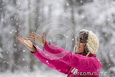 Happy young woman wearing warm hat and bright pink jacket standing outside in snowy nature Stock Photo