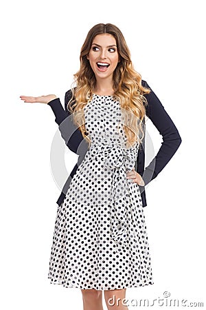 Happy Young Woman In White Dotted Dress And Cardigan Is Presenting Stock Photo