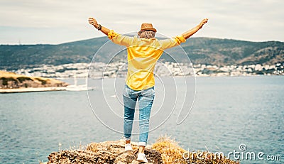 Happy young woman in a yellow shirt and hat rejoices on the seashore with a view, summer vacation and travel. Image with retro Stock Photo