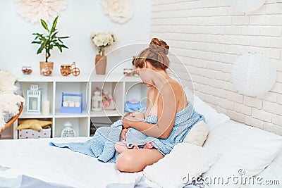 Happy young woman is breastfeeding while sitting and hugging her baby Stock Photo