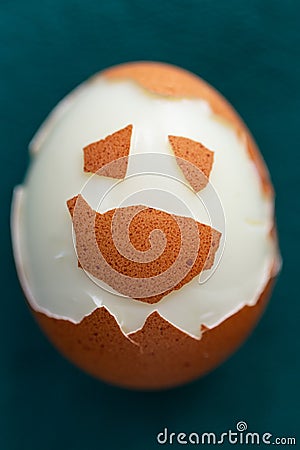 Hard-boiled half unshelled chicken egg on green background. Funny face made of eggshell on the surface. Stock Photo