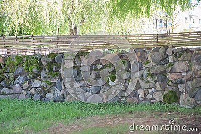 Long solid rural design fence made from aged stones and made decorative of bamboo Stock Photo