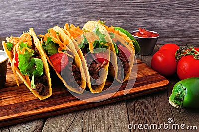 Hard shelled tacos with ground beef, vegetables and cheese, scene with wood background Stock Photo