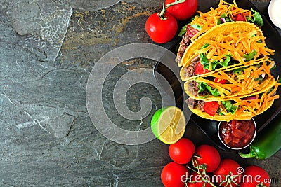 Hard shelled tacos with ground beef, vegetables and cheese, border on a dark background Stock Photo