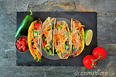 Hard shelled tacos with ground beef, vegetables and cheese, top view on a dark background Stock Photo
