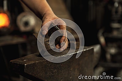Close-up working powerful hands of male blacksmith forge an iron product in a blacksmith. Hammer, red hot metal and Stock Photo