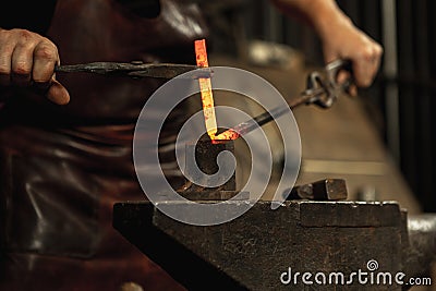 Close-up working powerful hands of male blacksmith forge an iron product in a blacksmith. Hammer, red hot metal and Stock Photo