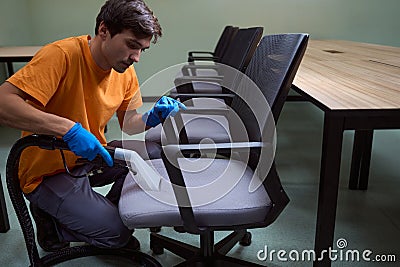 Hard-working janitor is deep-cleansing chairs with vacuum-cleaner Stock Photo