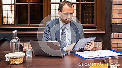 Hard working smiling businessman in restaurant with laptop and pad. Stock Photo